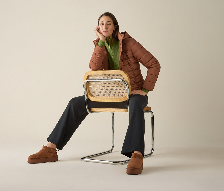 Kobieta siedzi na krześle w swetrze z kołnierzem typu troyer, kurtce i butach.