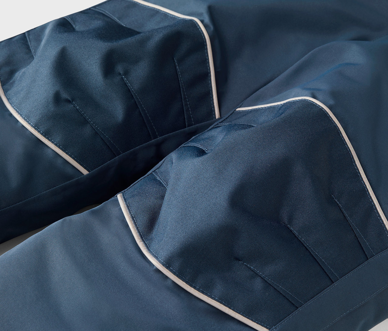 Szczegół niebieskich spodni z białą lamówką i kieszeniami.