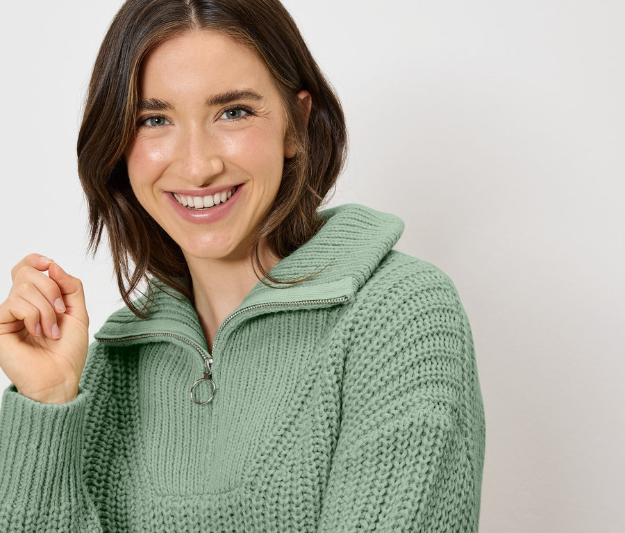 Uśmiechnięta kobieta ma na sobie jasnozielony sweter z zamkiem błyskawicznym.