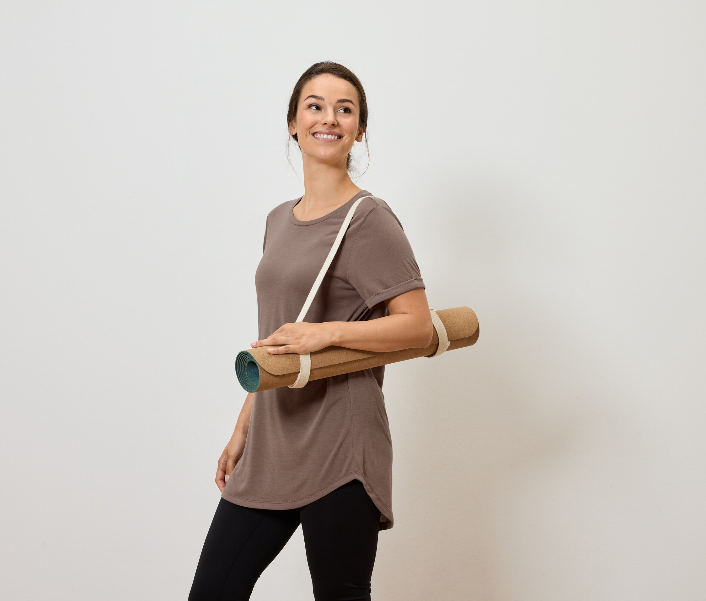 Uśmiechnięta kobieta nosi matę do jogi na ramieniu.