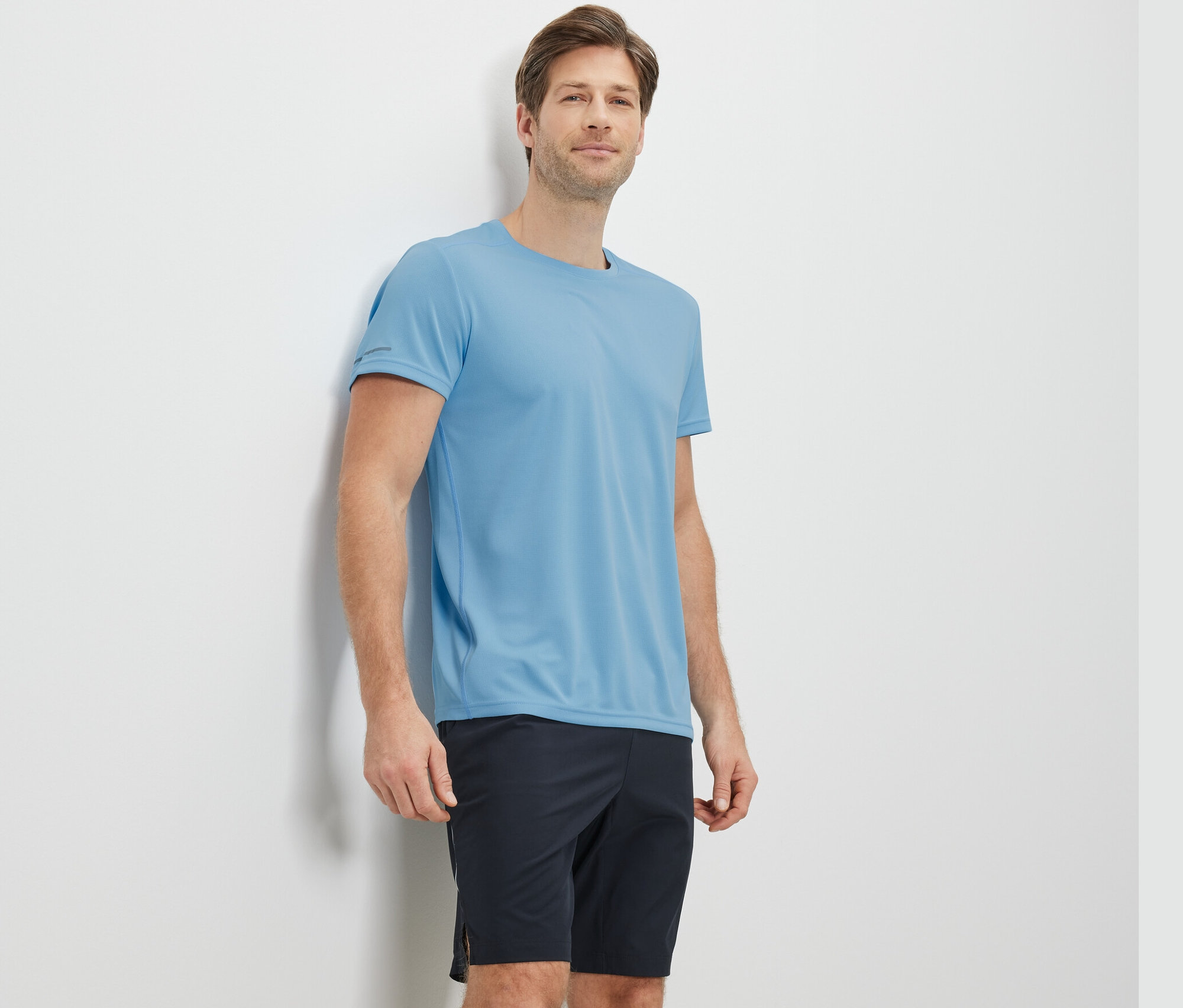 Mężczyzna oparty o ścianę w jasnoniebieskiej koszulce funkcyjnej.
