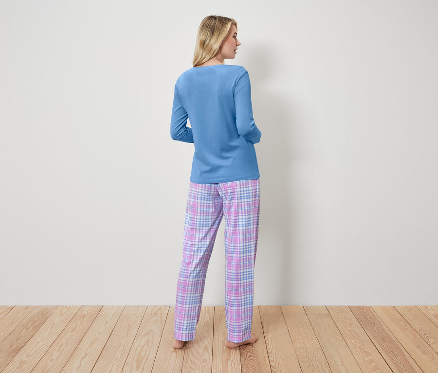 Kobieta w niebieskiej piżamie i spodniach w kratę stoi tyłem do kamery.