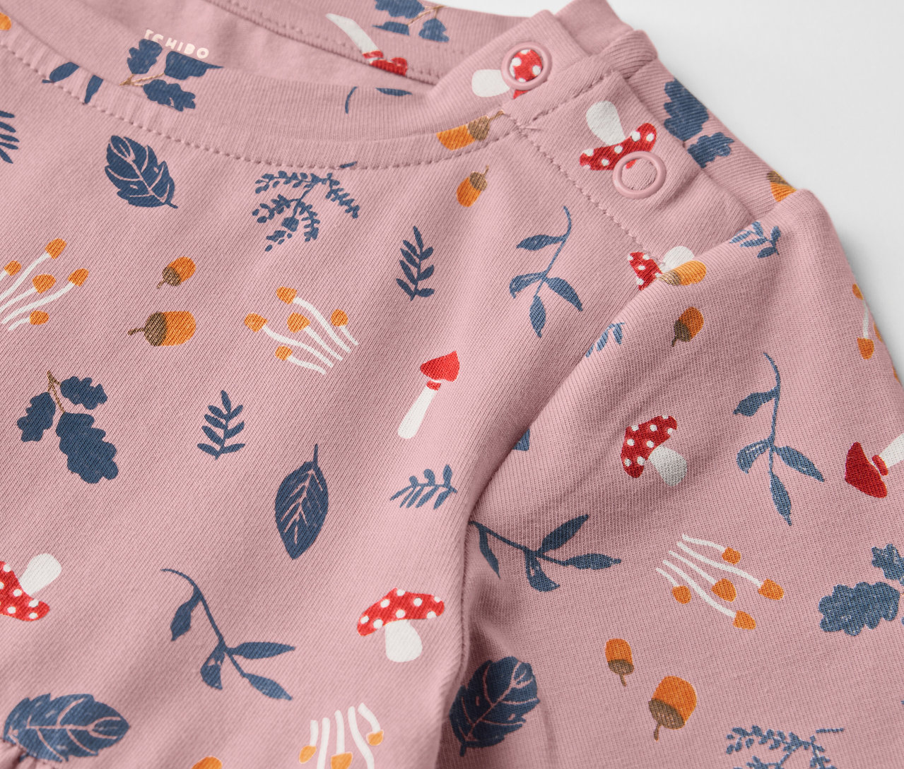 Zbliżenie na różową sukienkę dżersejową dla dzieci z nadrukiem liści i grzybów.