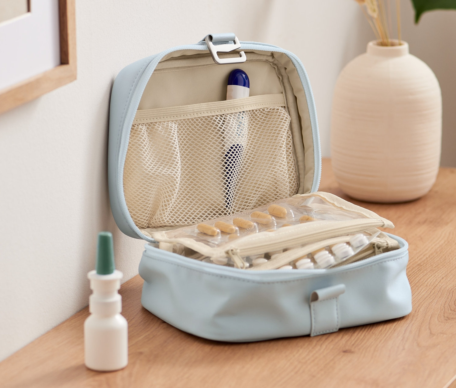 Otwarta, jasnoniebieska torba na lekarstwa z zawartością leków i butelek stoi na drewnianym stole.