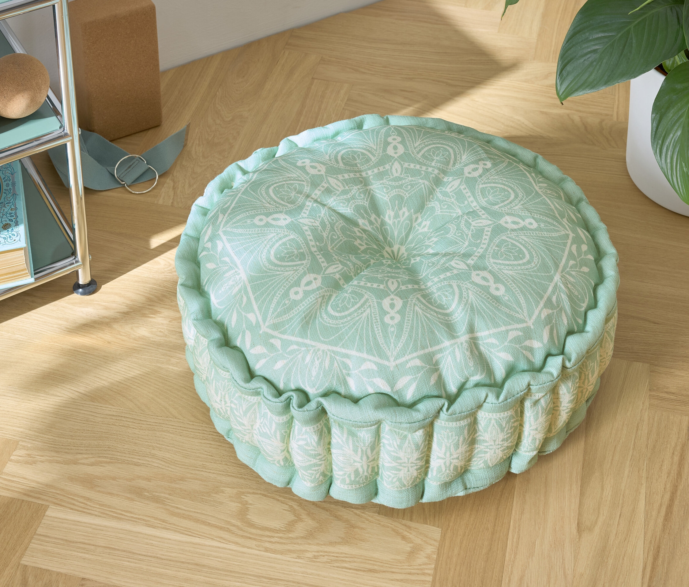 Zielona poduszka do siedzenia z białym wzorem na drewnianej podłodze.