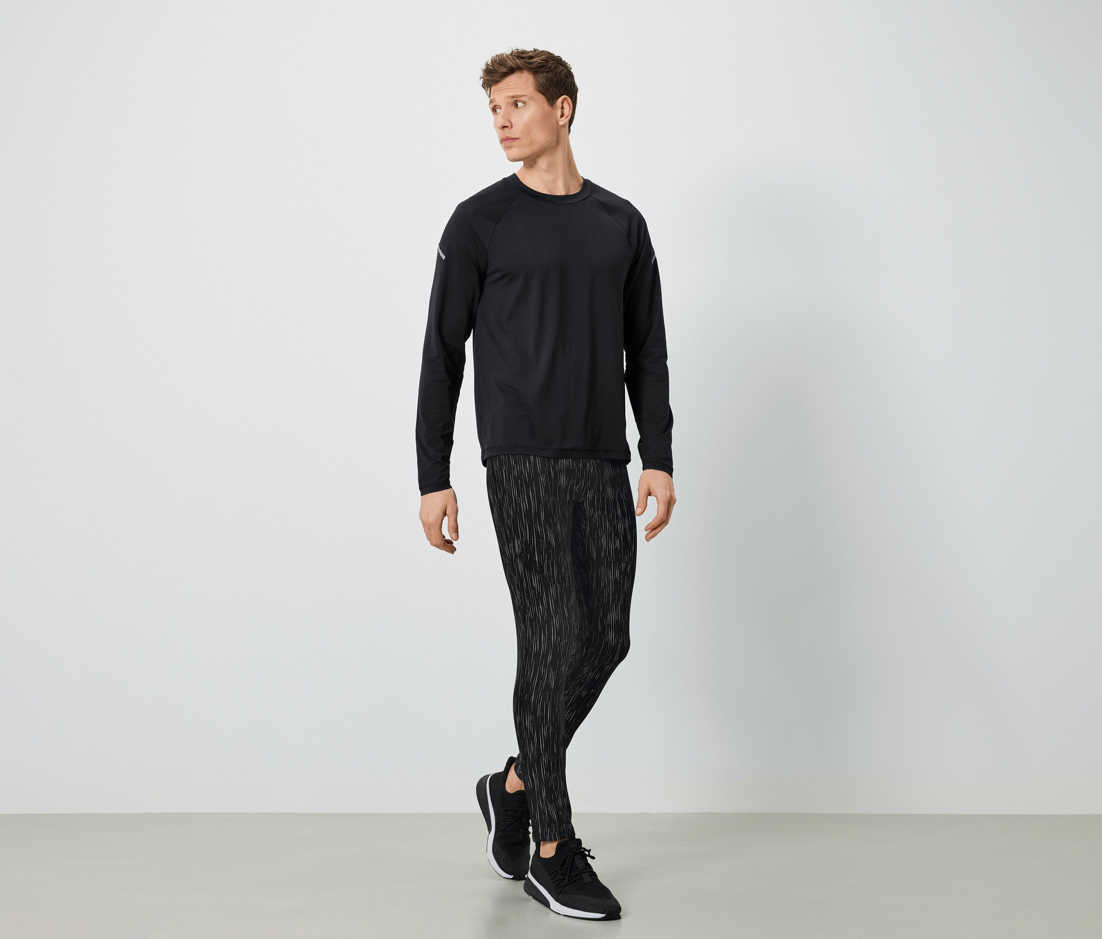 Mężczyzna w czarnym stroju sportowym pozuje na jasnym tle.