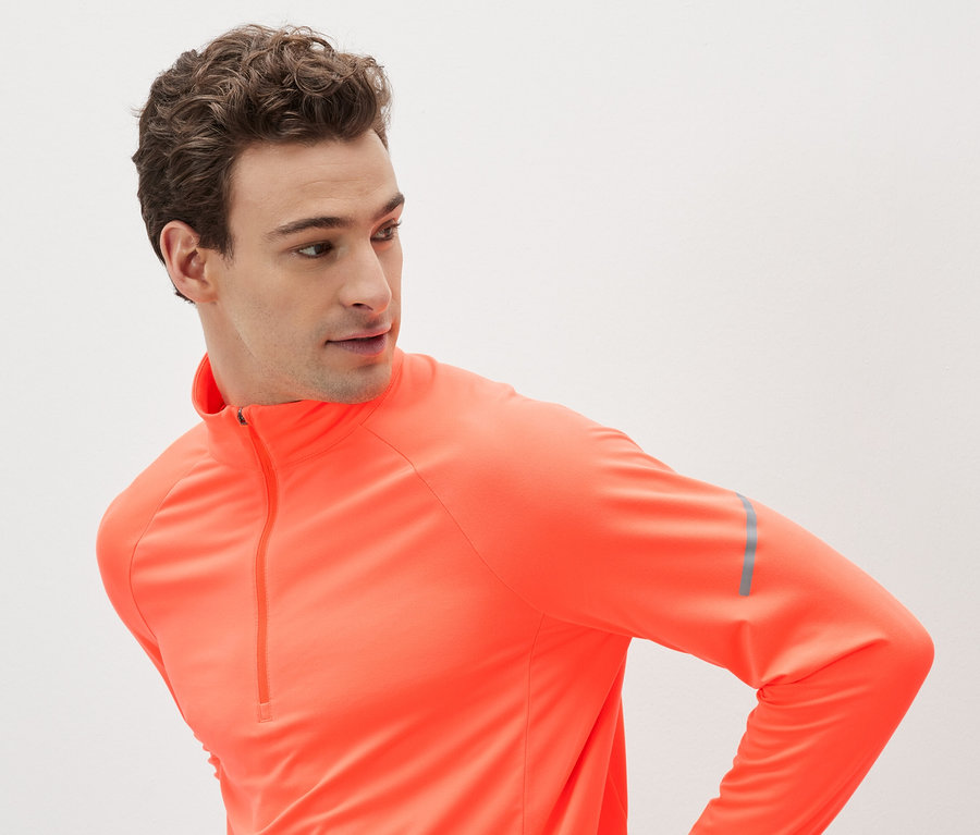 Mężczyzna w pomarańczowej koszulce sportowej z długim rękawem i zamkiem błyskawicznym.