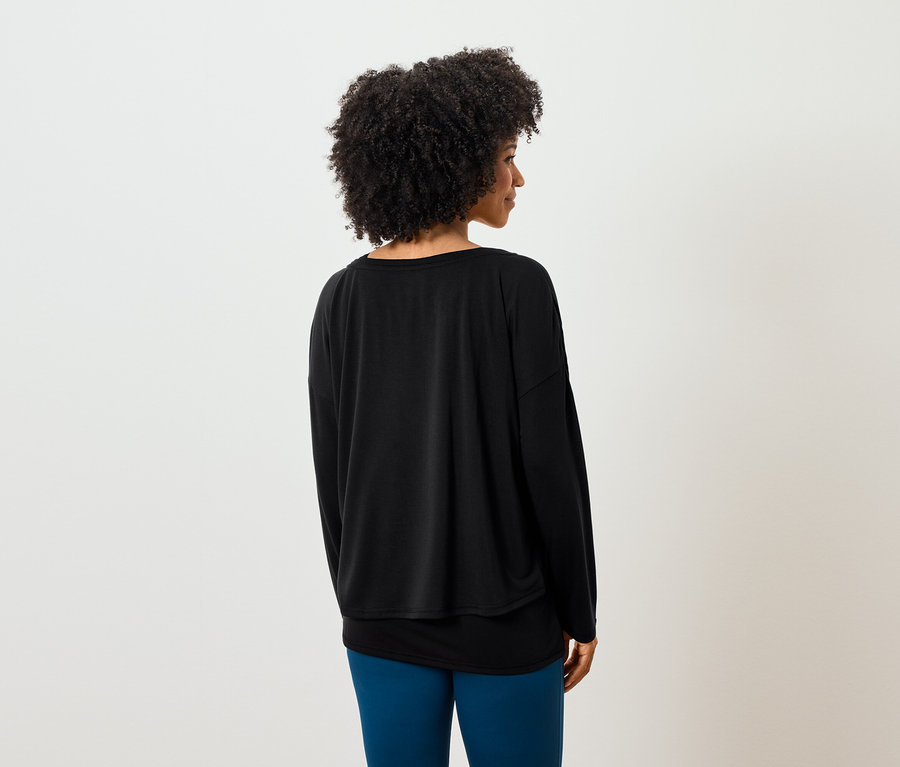 Z tyłu widać kobietę z kręconymi włosami, ubraną w czarną bluzkę z długim rękawem i niebieskie legginsy.