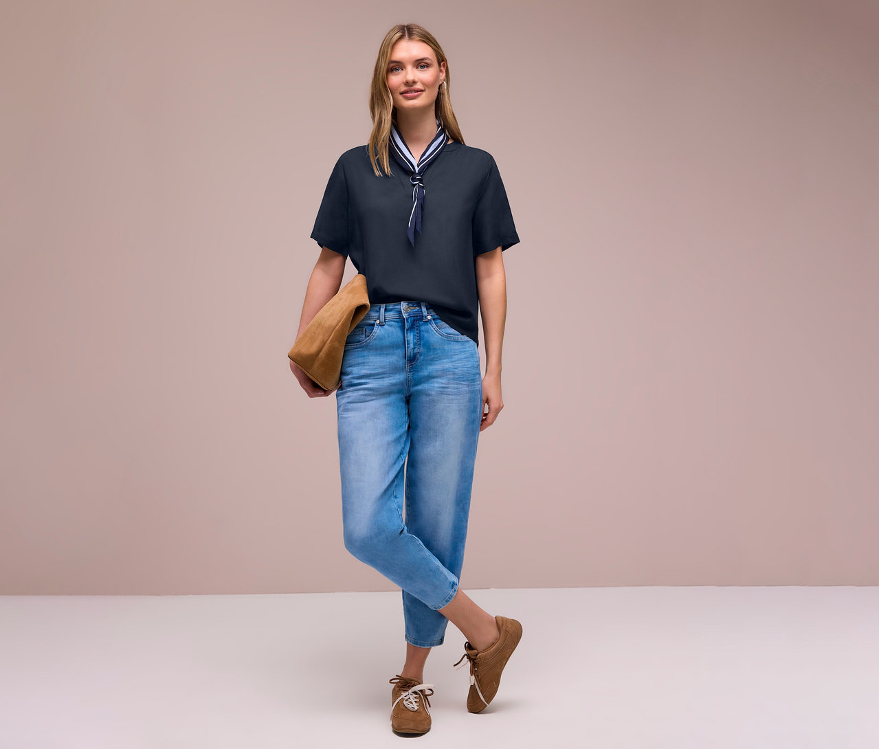 Kobieta w dżinsach i brązowych butach z torbą, ma na sobie bluzkę z tkaniny Street One z apaszką.