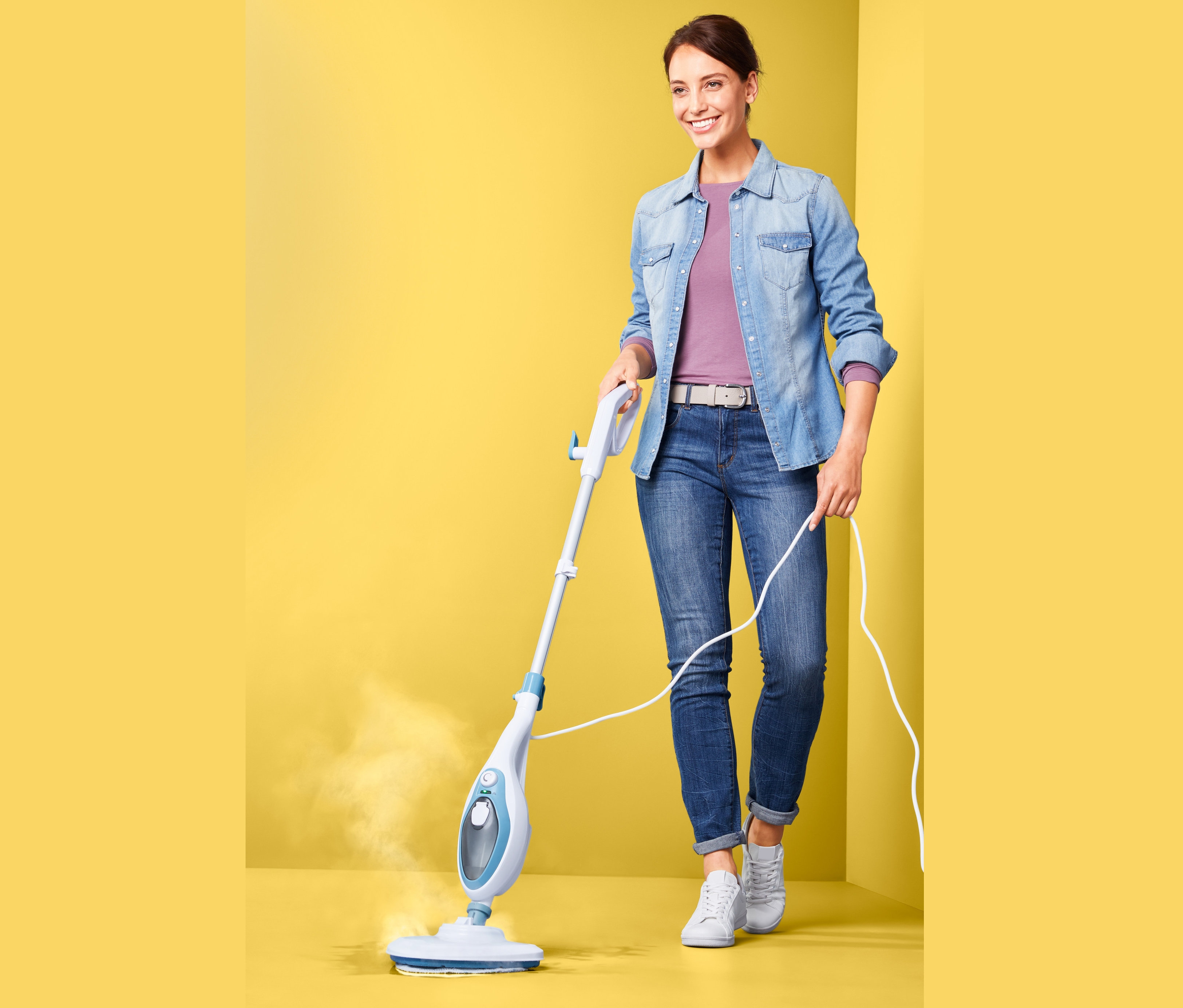 Kobieta używa wielofunkcyjnej myjki parowej na żółtym tle.