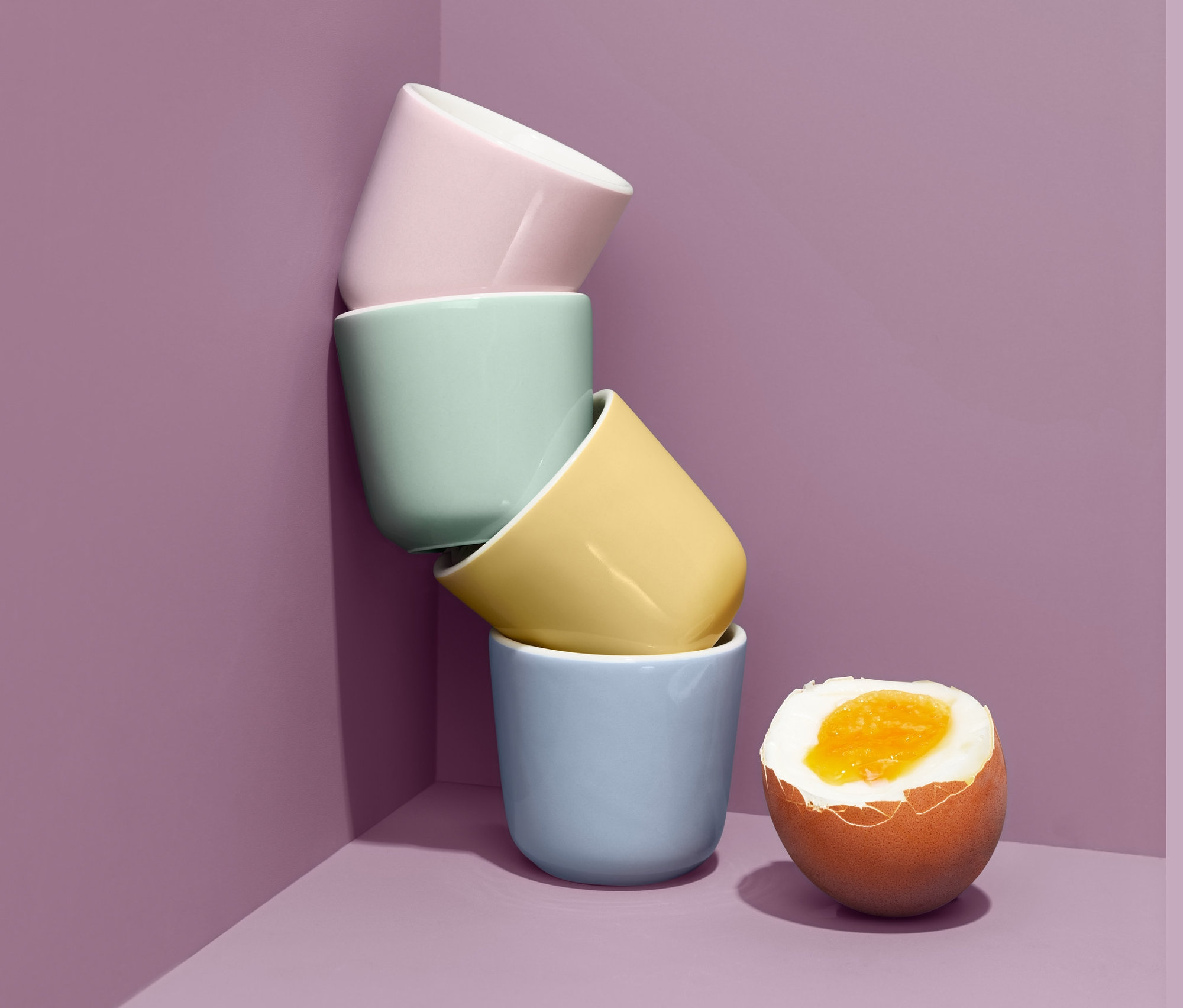 Cztery pastelowe ceramiczne podstawki do jajek ułożone jeden na drugim obok ugotowanego jajka.
