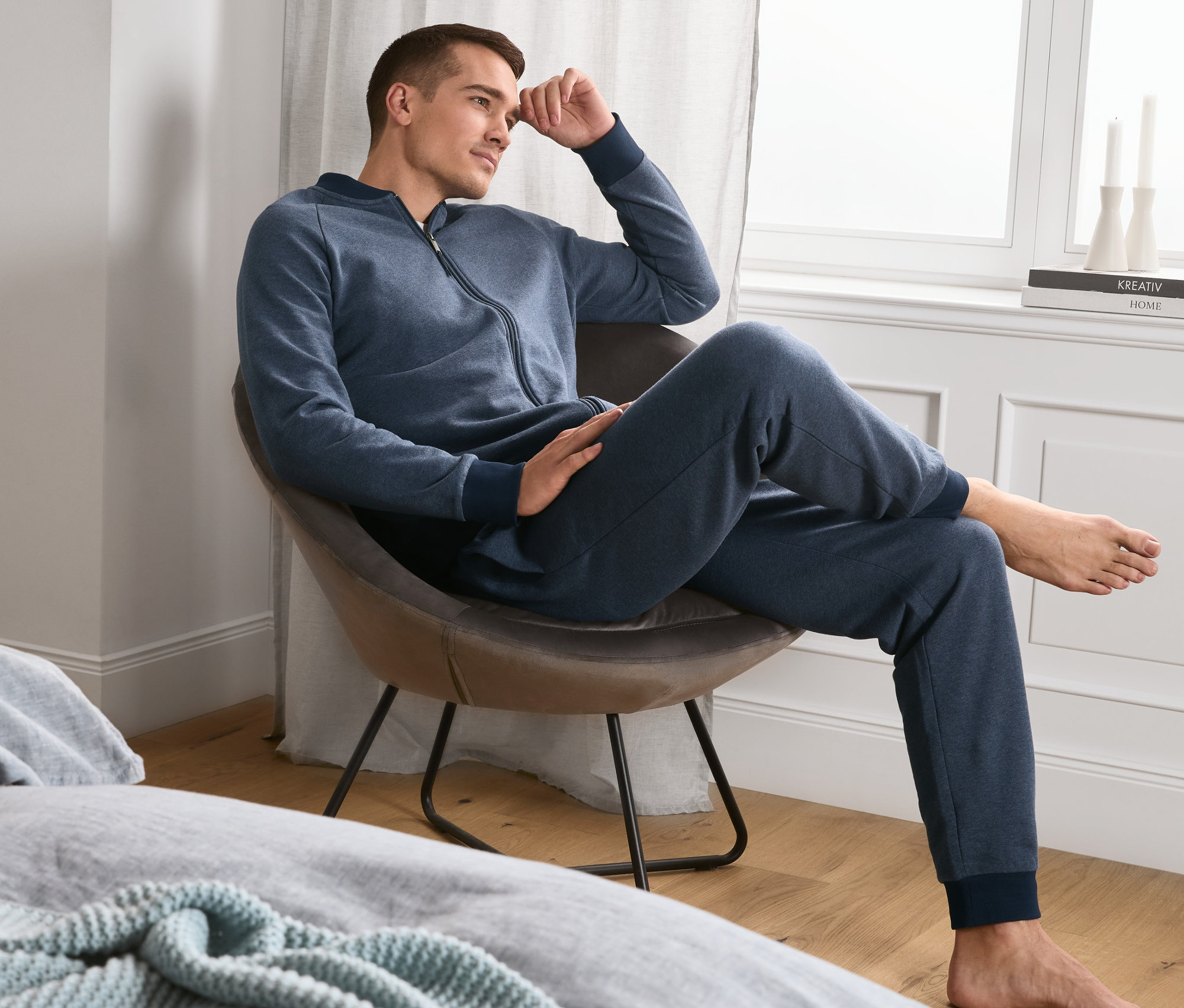Mężczyzna siedzi w fotelu ubrany w niebieski dres domowy z miękkiej dzianiny dresowej.