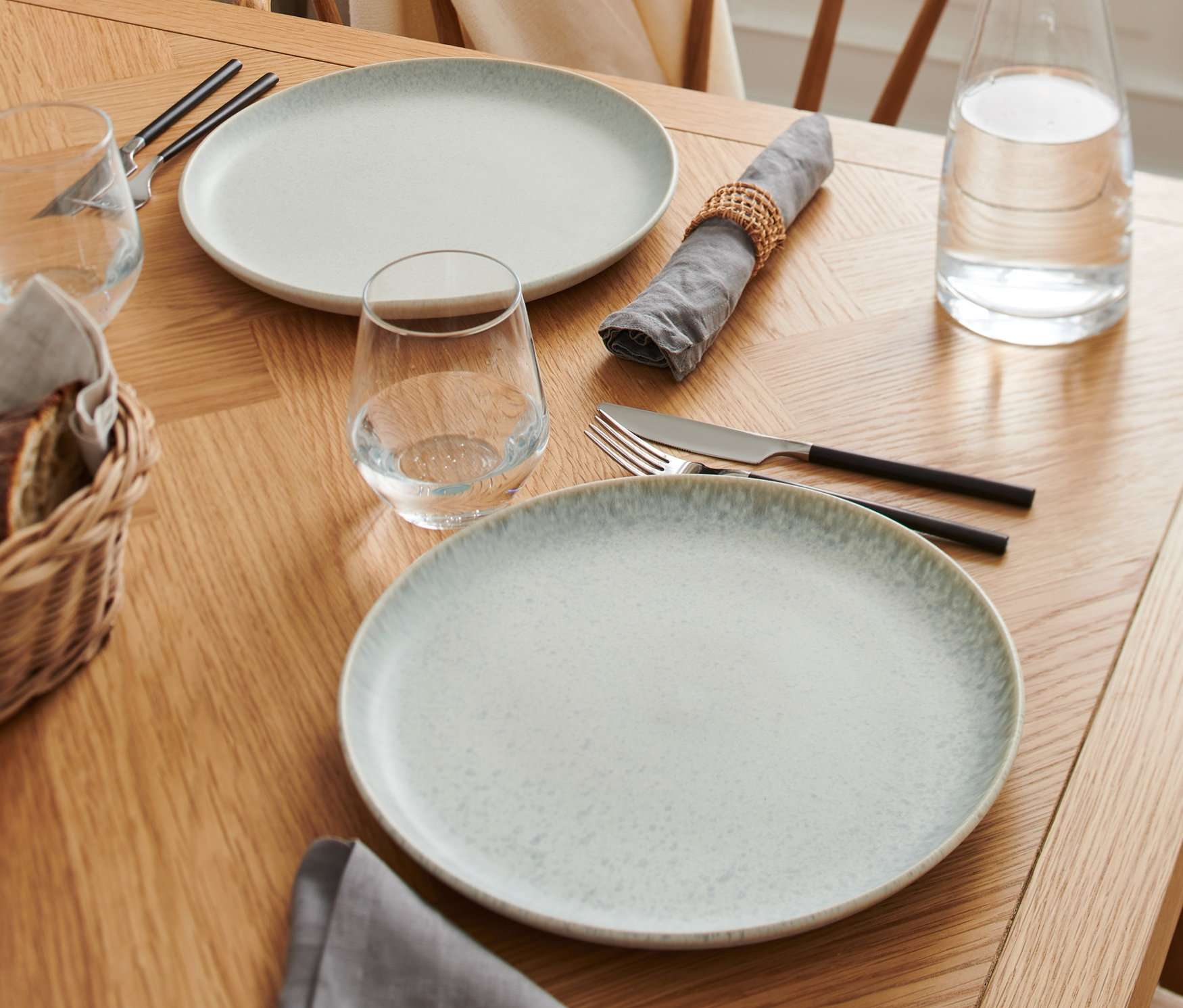 Dwa talerze na drewnianym stole z serwetkami i szklankami.