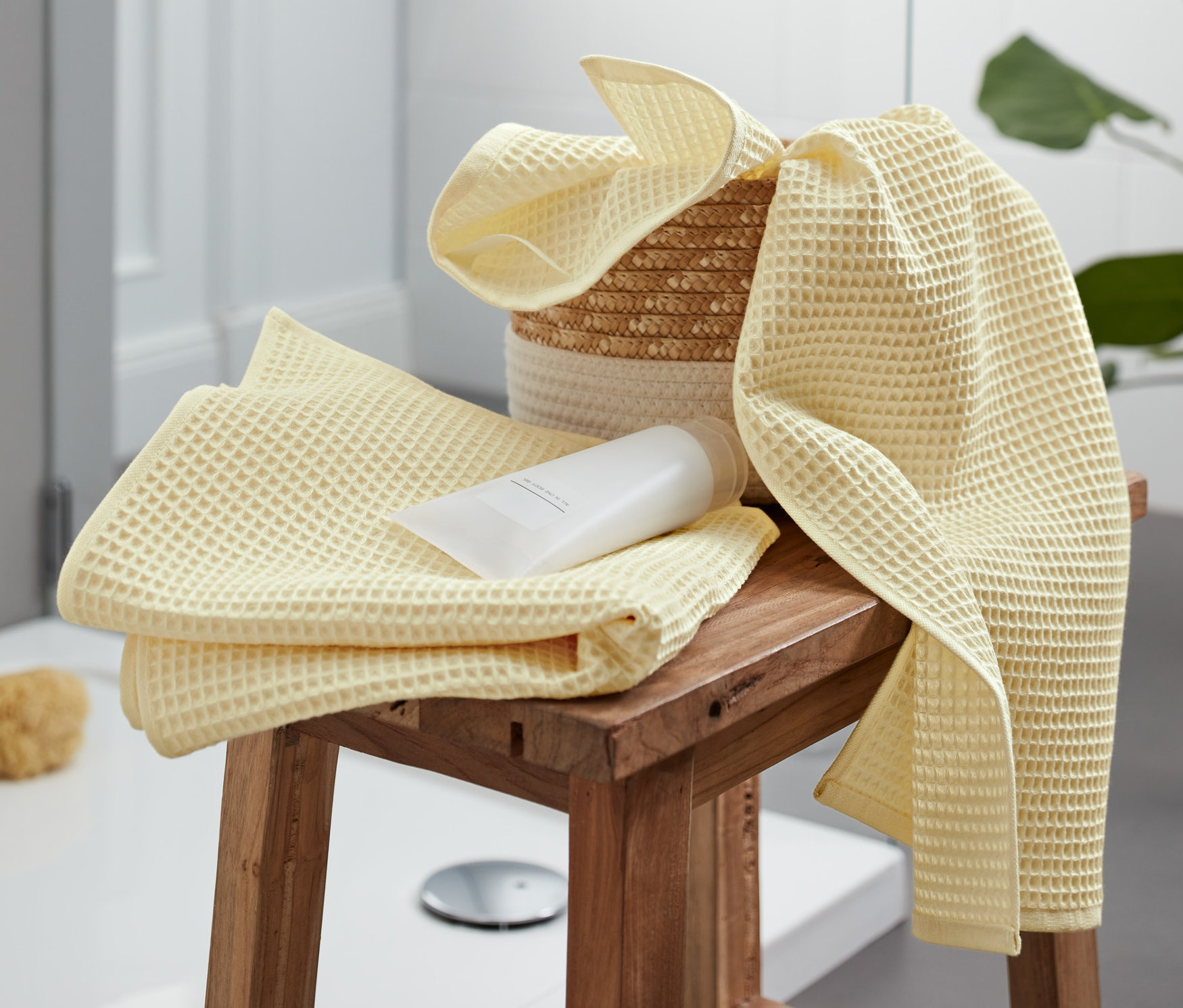 Waniliowe ręczniki premium o splocie waflowym (2 szt.) leżą na drewnianym stołku w łazience.