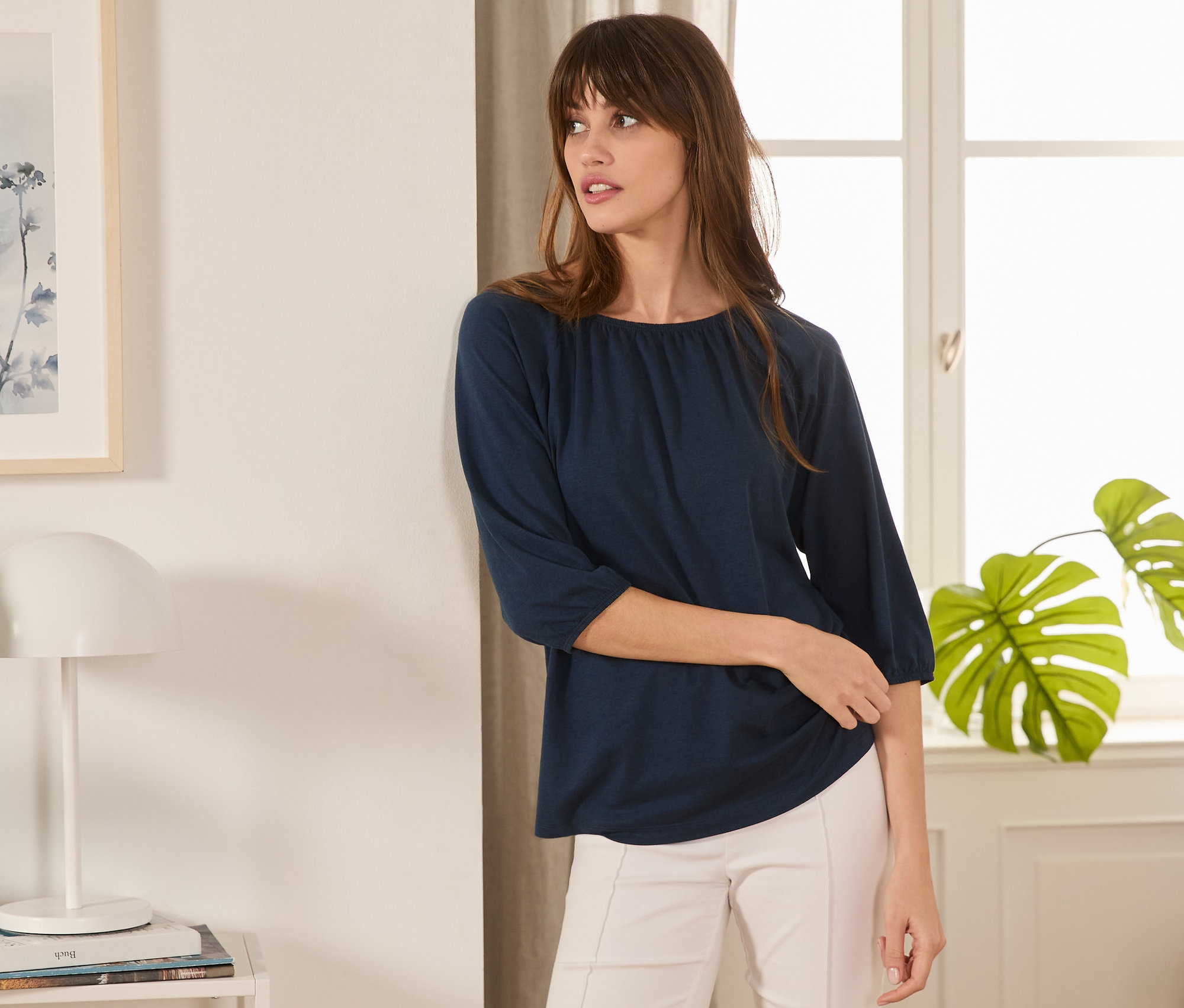 Kobieta pozuje w granatowej bluzce z rękawami o długości 3/4.