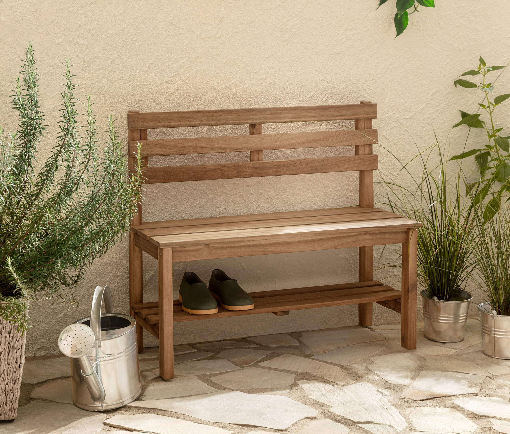 Dwie wysokie donice z naturalną plecionką w jodełkę stoją obok małej ławki ogrodowej »Lenja« z półką.