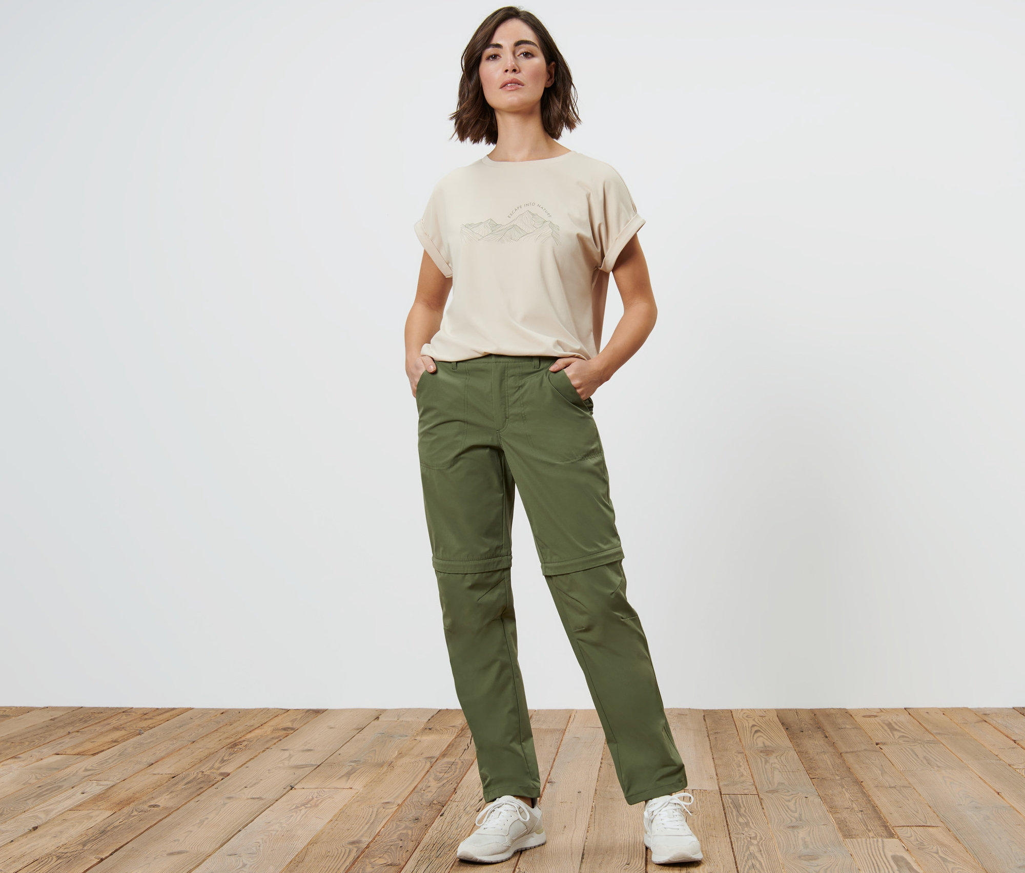 Kobieta stoi z rękami w kieszeniach khaki spodni funkcyjnych 2 w 1.