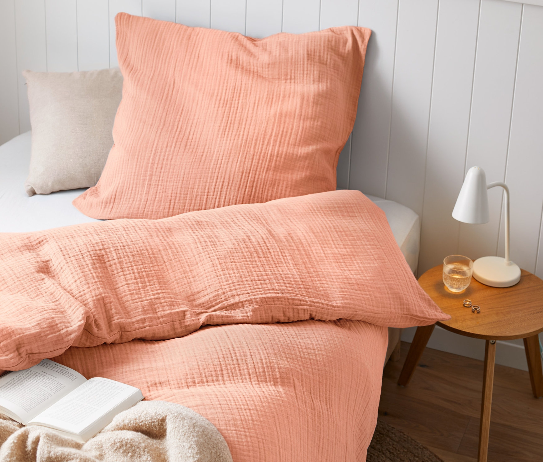 Pościel muślinowa w rozmiarze standardowym i niestandardowym na łóżku z książką i lampą.