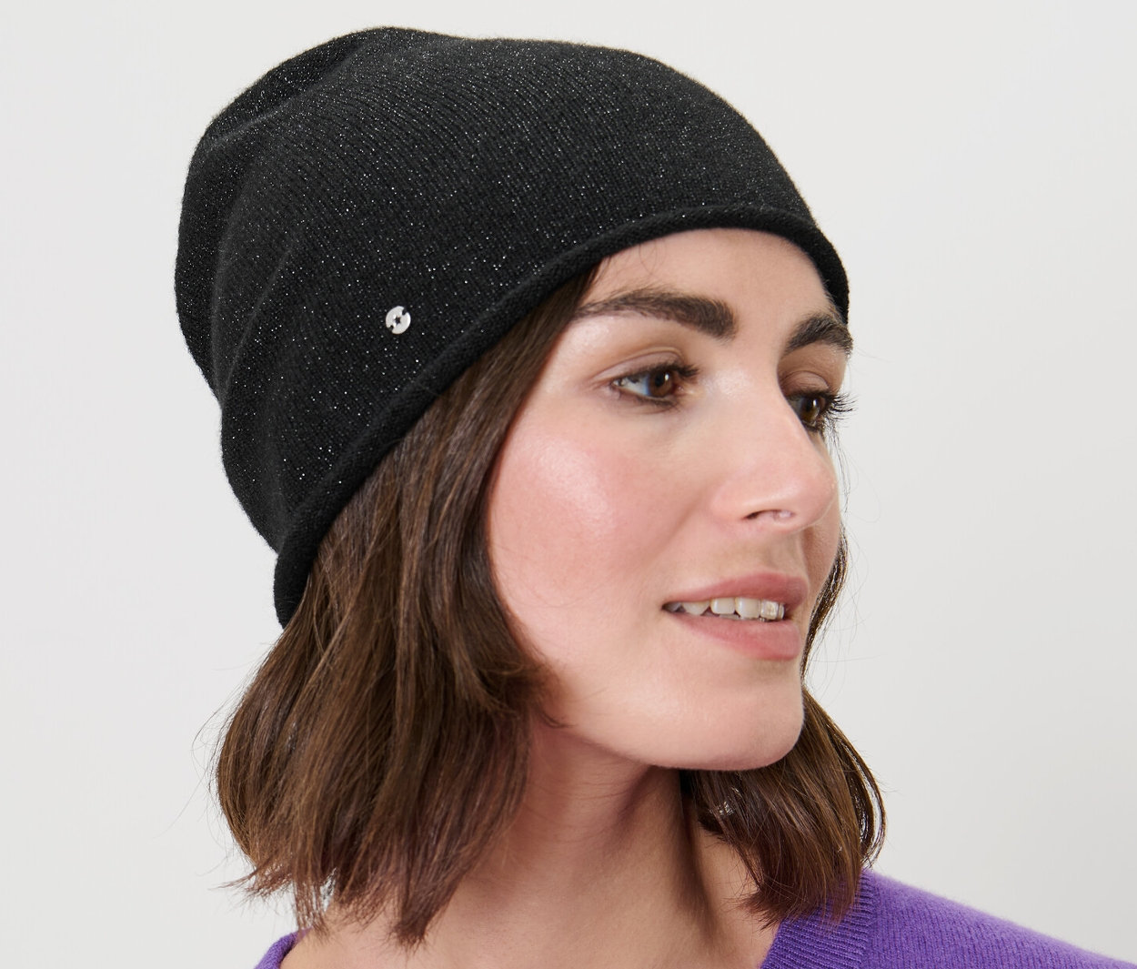 Kobieta z brązowymi włosami nosi błyszczącą czapkę z delikatnej dzianiny w kolorze czarnym.