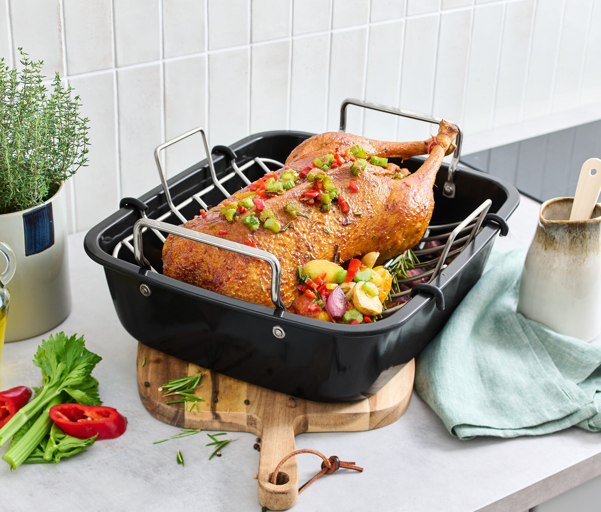 Pieczona kaczka w brytfannie XL ze stali nierdzewnej z rusztem, na stole z warzywami i ziołami.