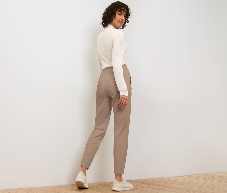 Kobieta patrzy przez ramię, ubrana w beżowe spodnie dresowe.