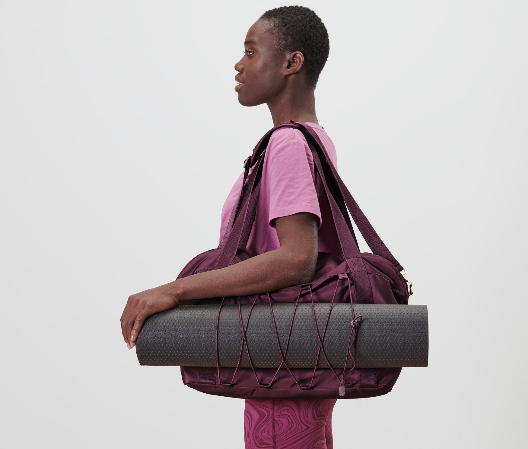 Kobieta niosąca torbę sportową i matę do jogi.