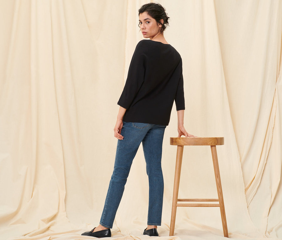 Kobieta pozuje w czarnym swetrze z delikatnej dzianiny, dżinsach slim »Fit Emma«, mid blue denim i skórzanych półbutach.
