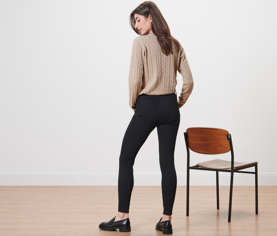 Kobieta stoi tyłem do kamery, ubrana w beżowy sweter i jegginsy.