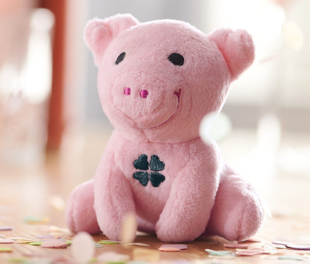 Siedząca, różowa chrumkająca świnka na szczęście z koniczyną na brzuchu, otoczona konfetti.