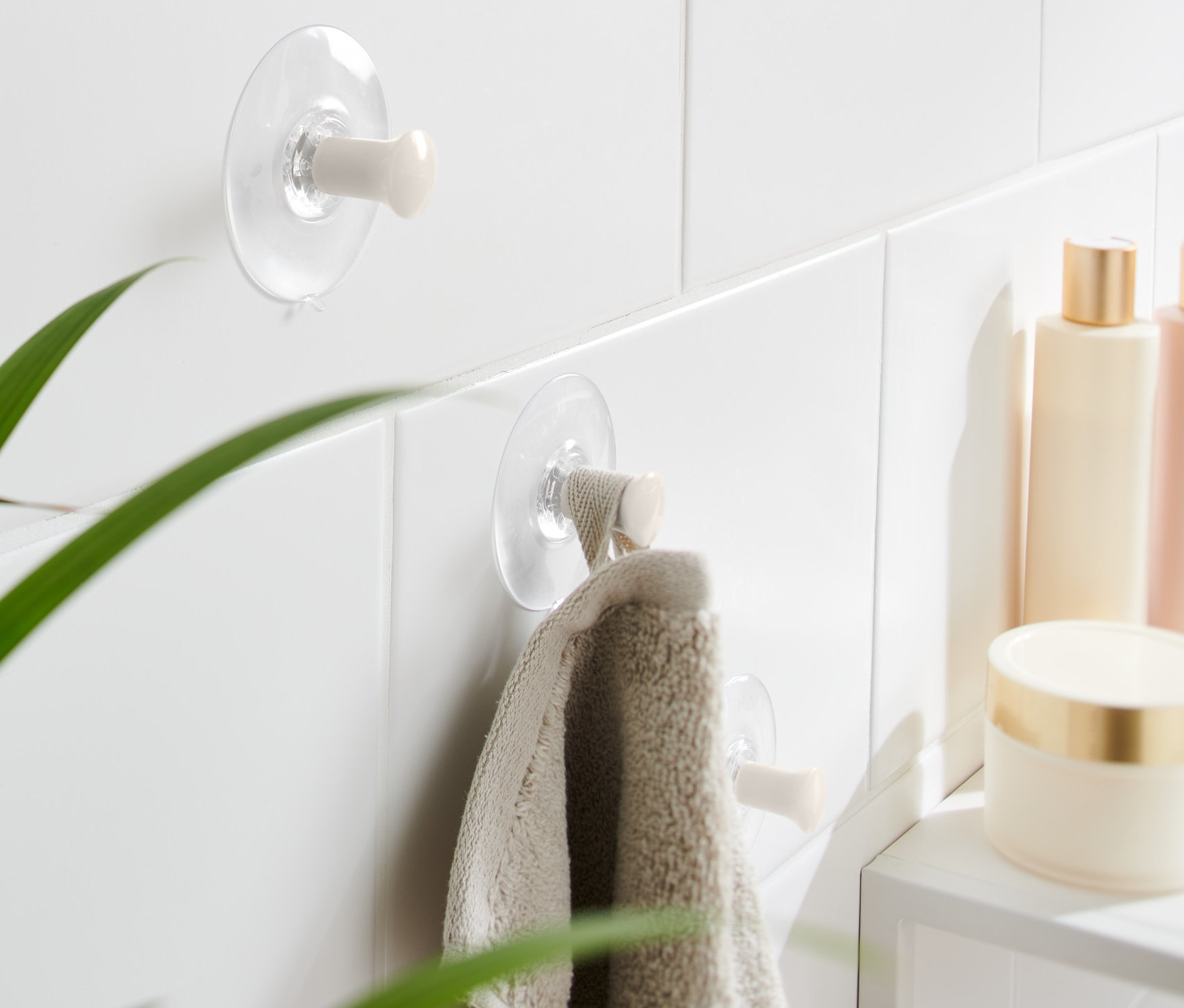 Dwa haczyki z przyssawką, 3 sztuki, przymocowane są do białych płytek, na jednym z nich wisi ręcznik.