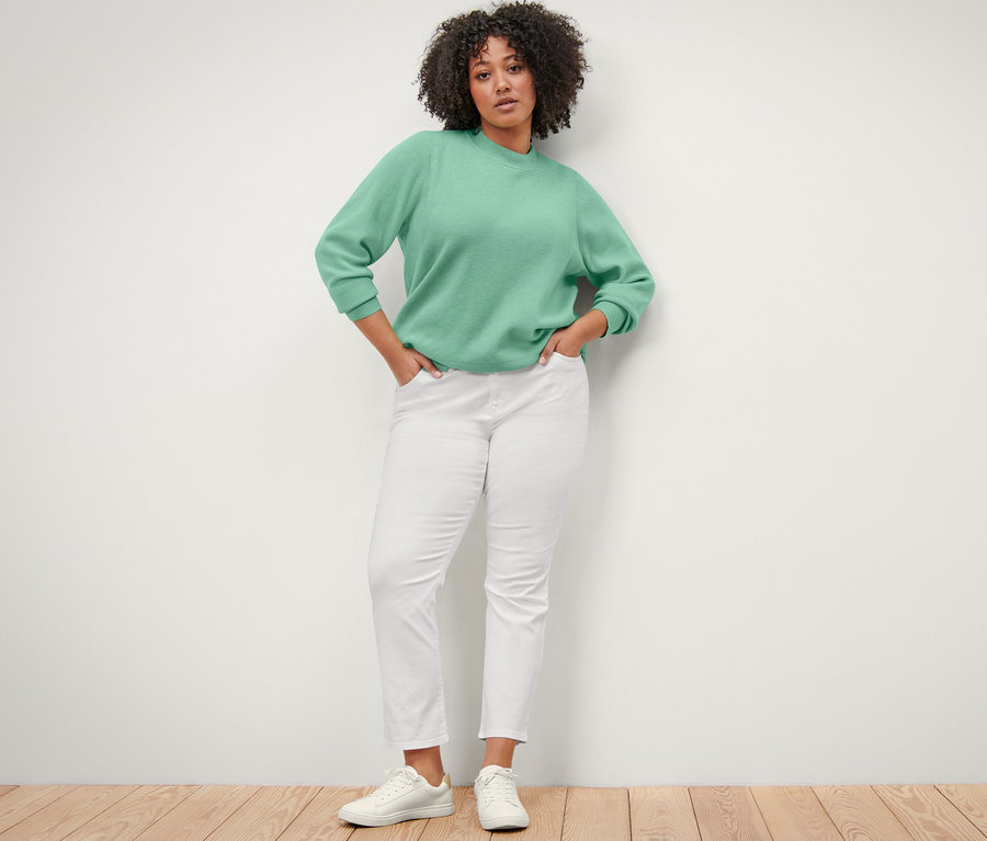 Kobieta pozuje w swetrze z dzianiny i kremowych spodniach dżinsowych „Emma”.