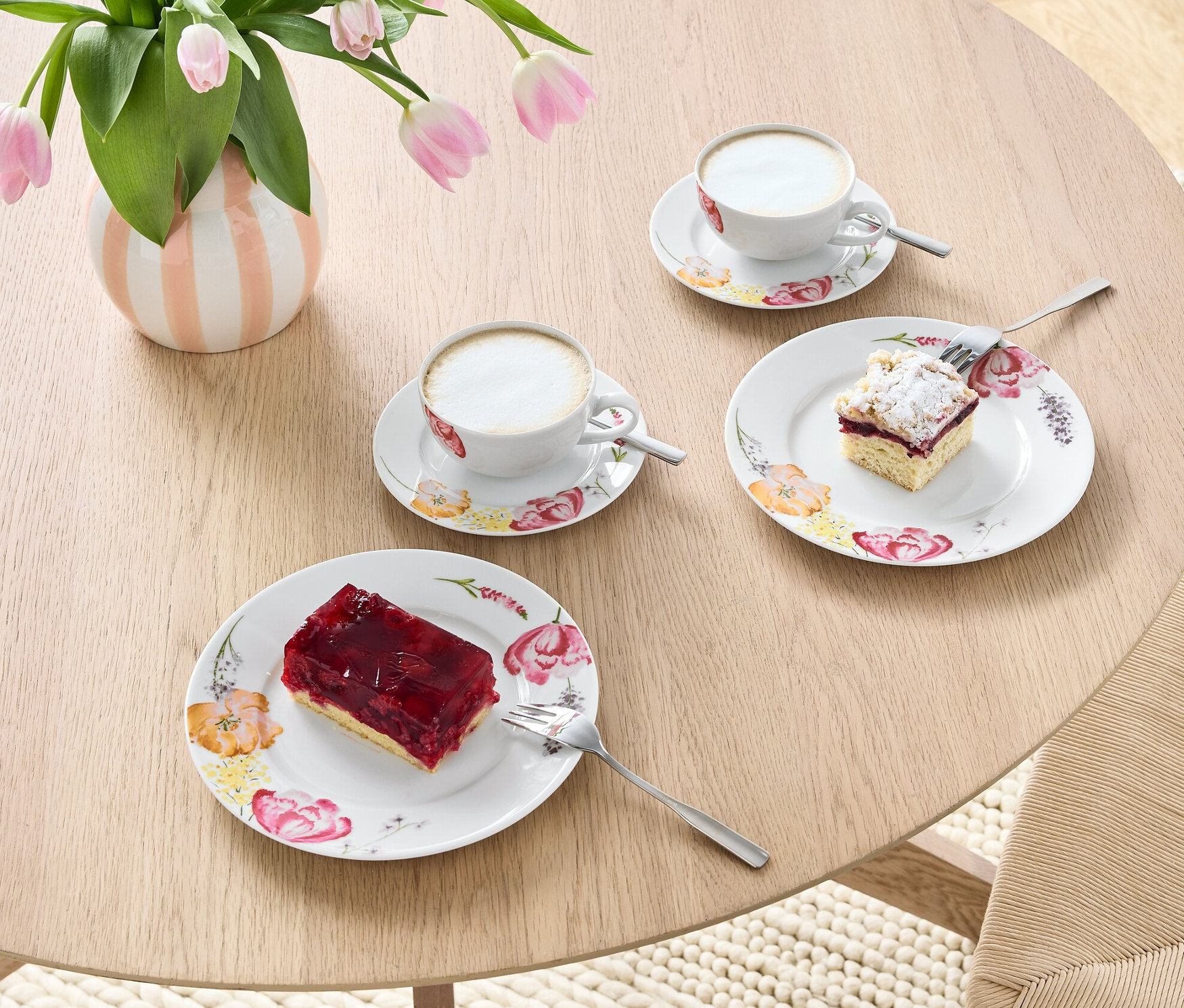 Na stole stoi wazon z tulipanami i 6-częściowy serwis do kawy z kawą i ciastami.