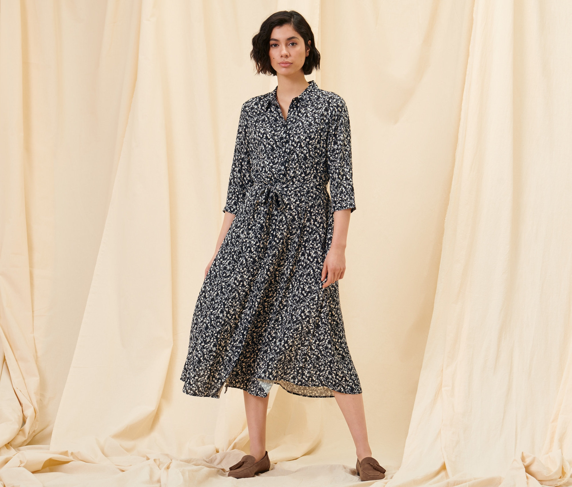 Kobieta pozuje w sukience koszulowej w kwiaty i półbutach ze skóry welurowej.