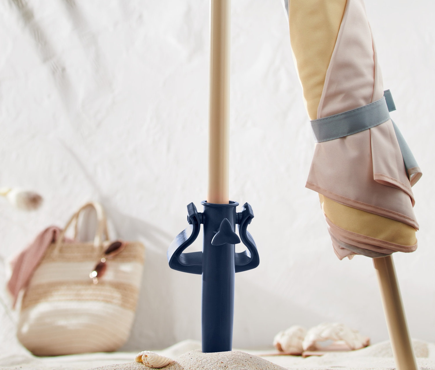 Parasol w pastelowe paski jest przymocowany do niebieskiego wkręcanego uchwytu na parasol plażowy w piasku.