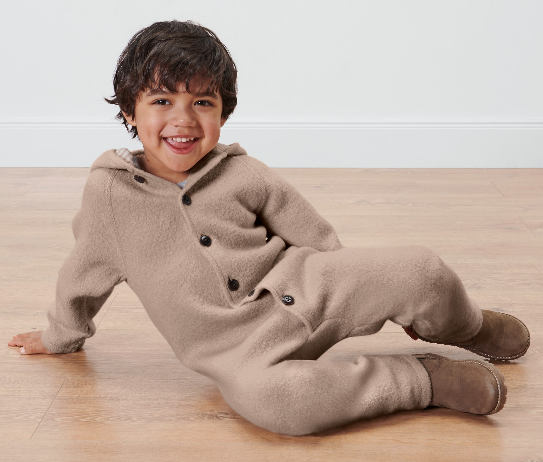 Chłopiec leży na podłodze w brązowym kombinezonie dziecięcym z wełny merino.