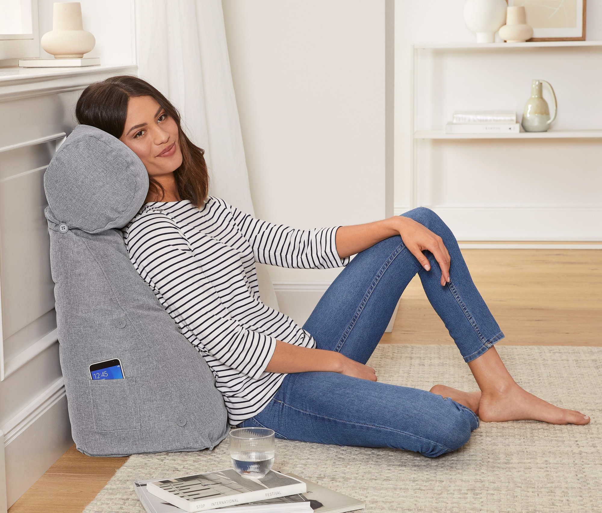 Kobieta siedzi oparta o szarą poduszkę pod plecy z wałkiem pod kark.