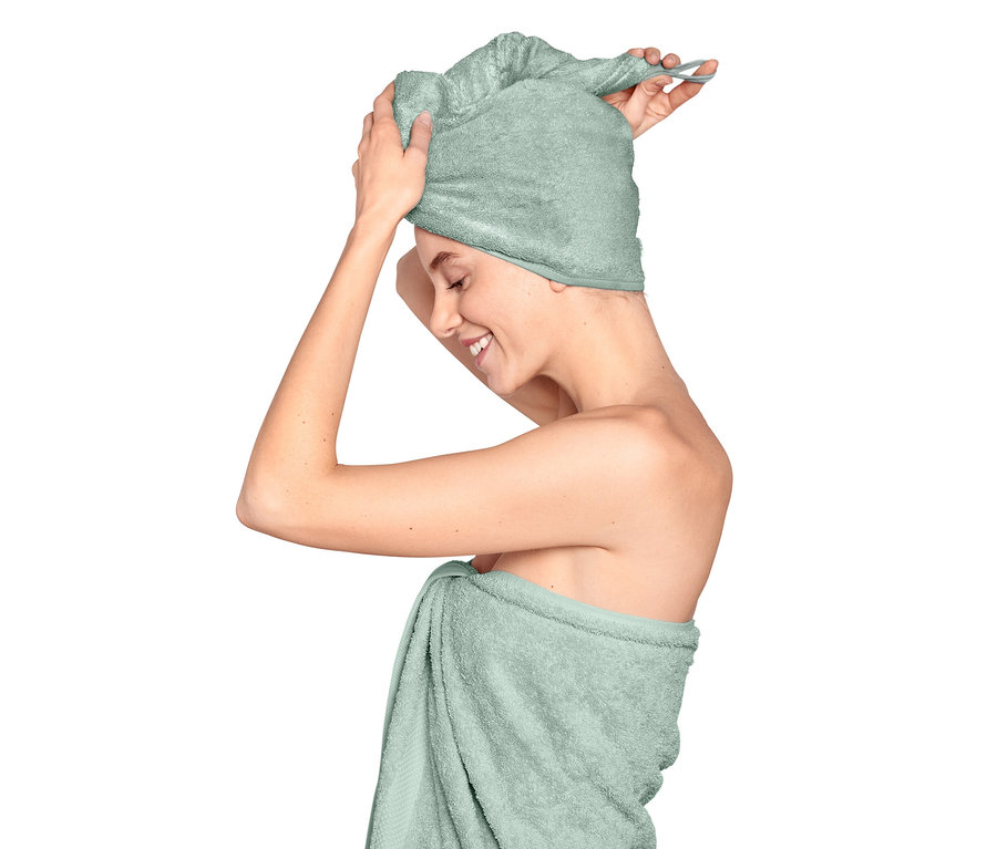 Kobieta zakłada jasnoniebieski ręcznik turban na głowę.