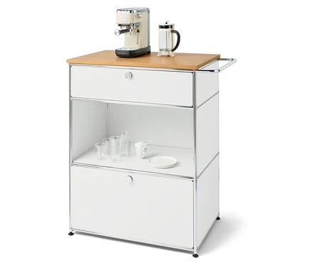 Ekspres do kawy i french press na białej komodzie z szufladami i półką ze szklankami i talerzem.