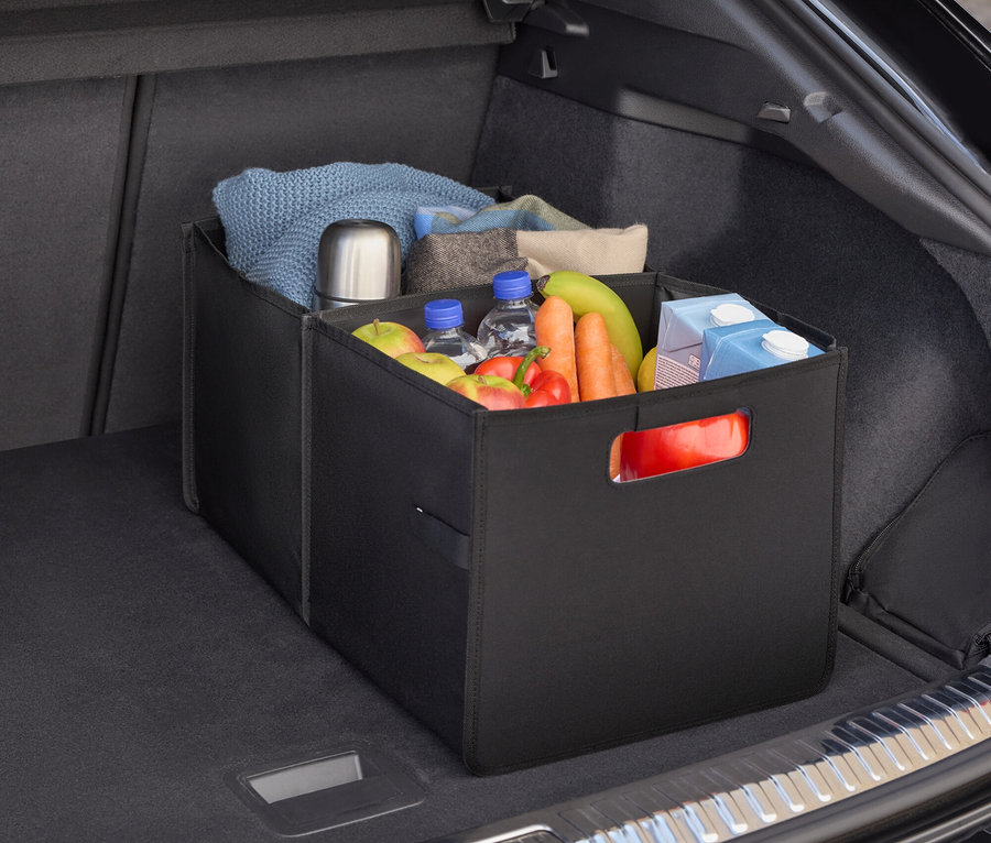 W bagażniku samochodu znajduje się czarny organizer wypełniony jedzeniem, butelkami wody, owocami i warzywami.