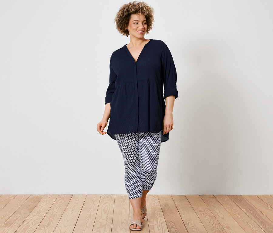 Kobieta ma na sobie długą bluzkę i wzorzyste legginsy o długości 3/4.