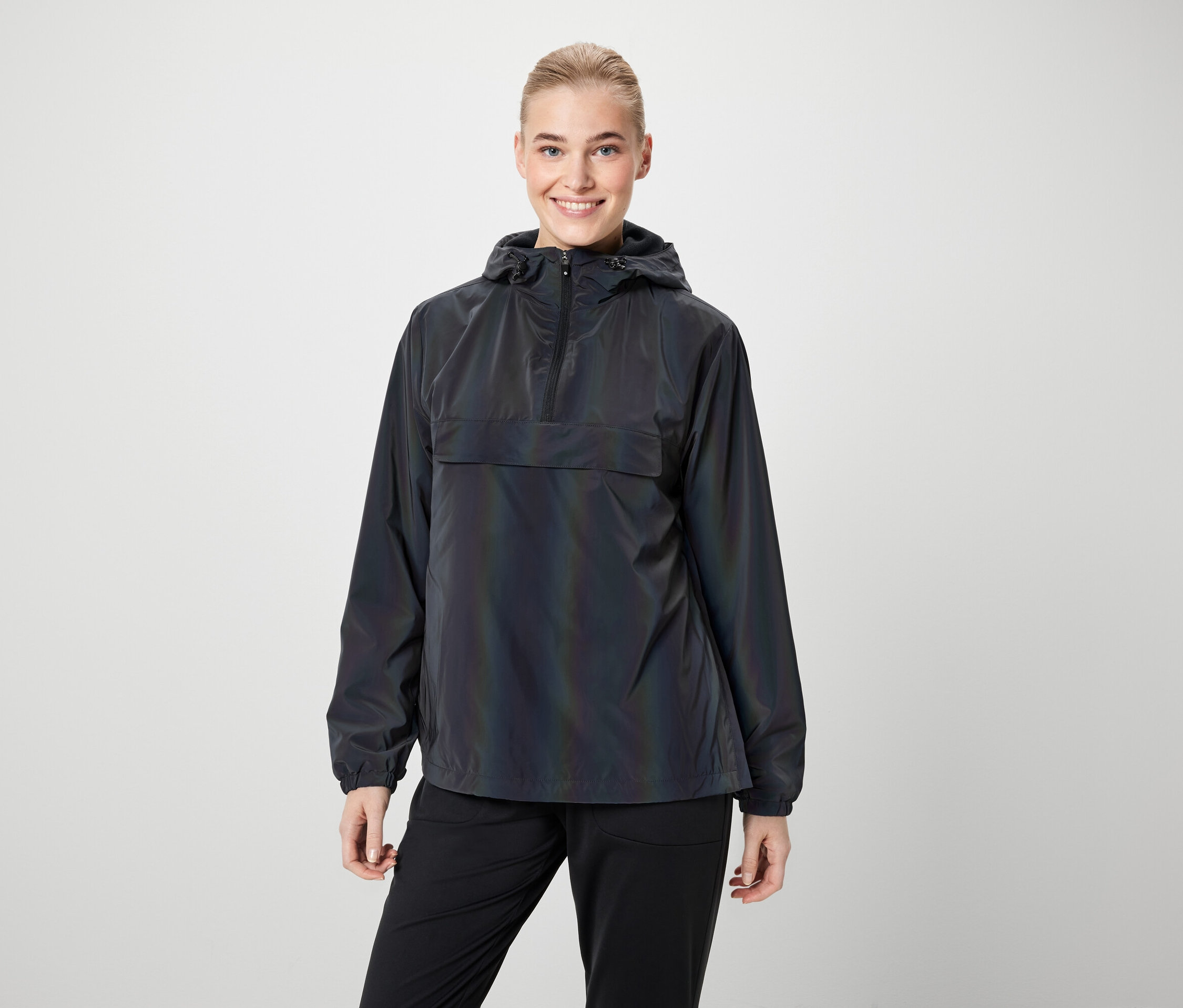 Kobieta ma na sobie tęczową kurtkę z kapturem i czarne spodnie.