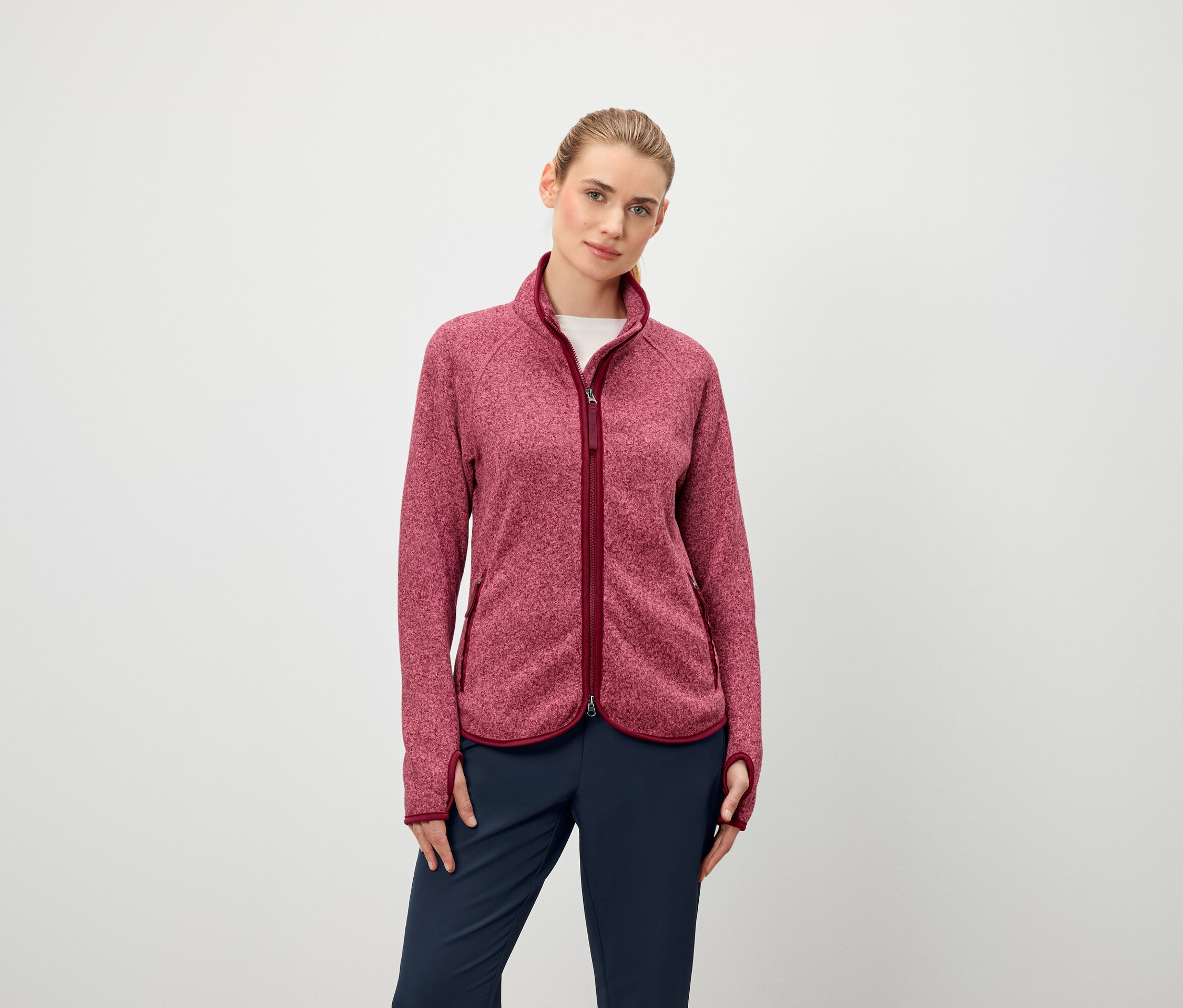 Kobieta ma na sobie bluzę polarową z długim rękawem zapinaną na zamek błyskawiczny i granatowe spodnie.
