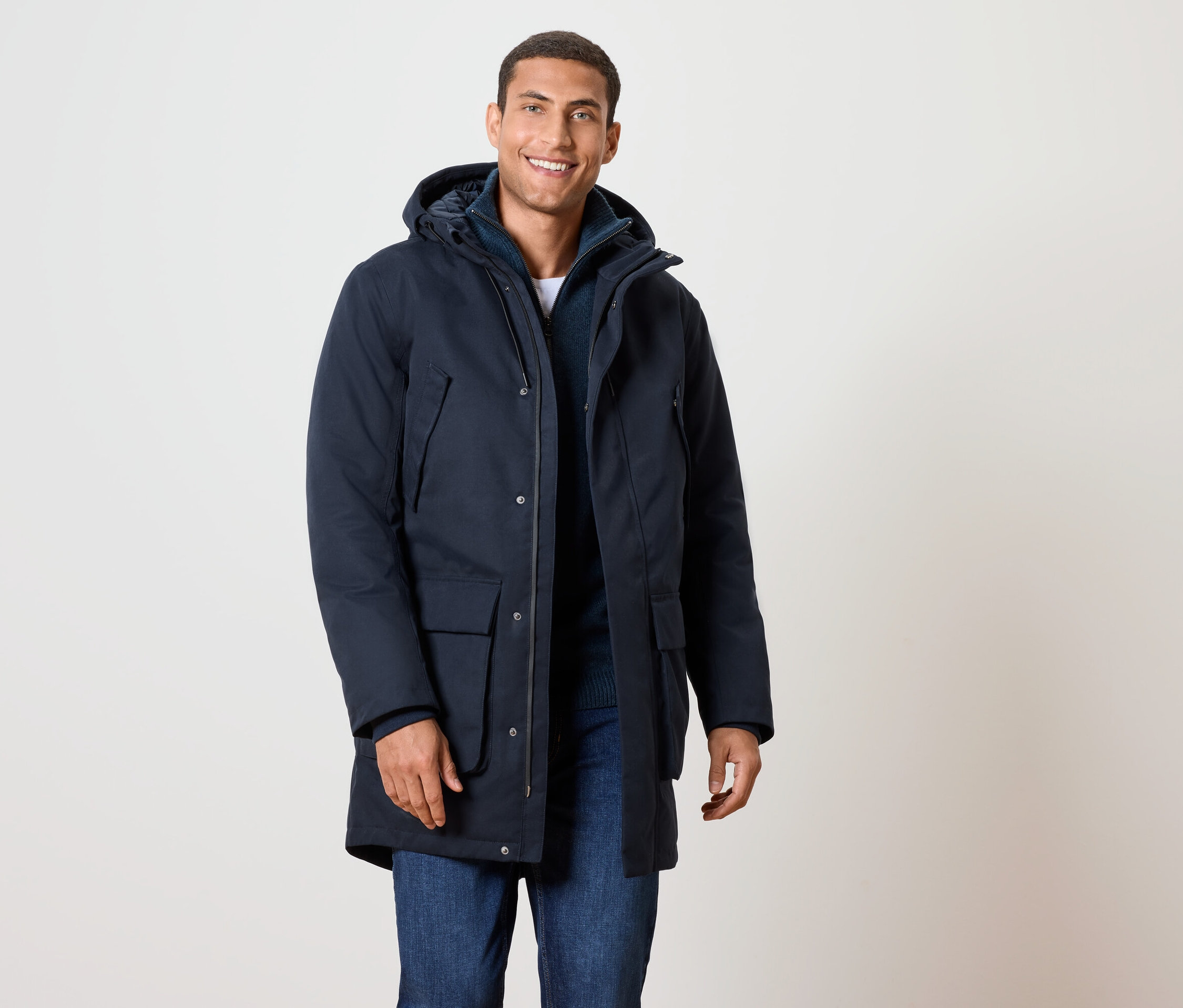 Uśmiechnięty mężczyzna w granatowej kurtce zimowej z kapturem i dżinsach.