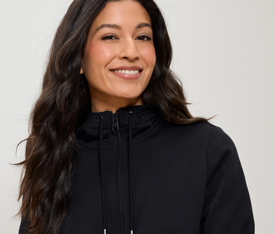 Portret kobiety z długimi brązowymi włosami, ubranej w czarną bluzę z kapturem na zamek błyskawiczny.