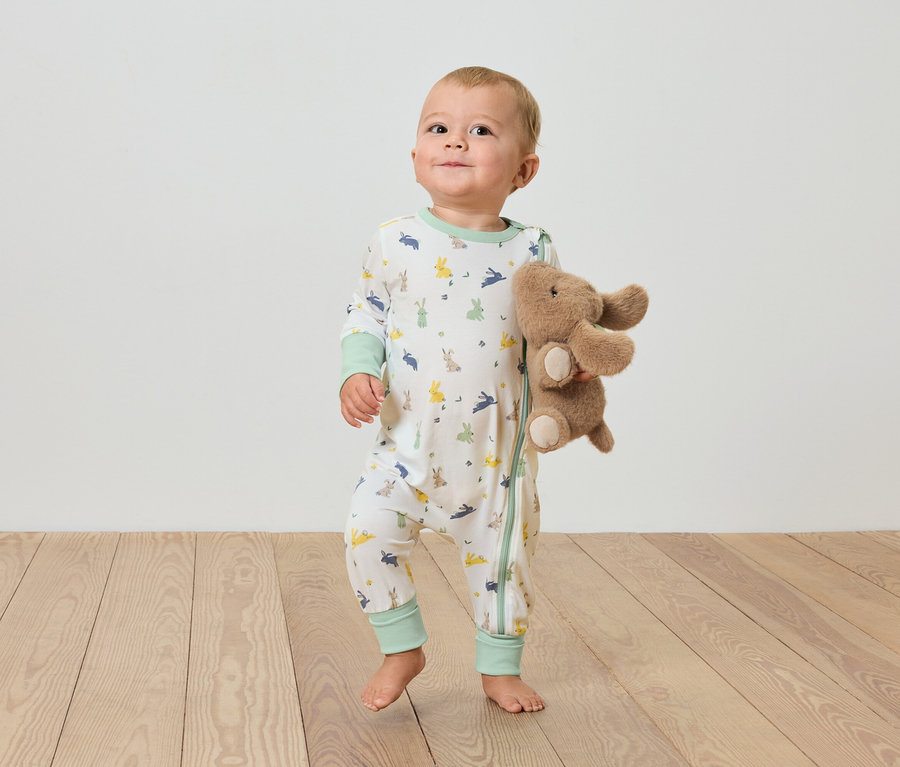 Dziecko stoi na drewnianej podłodze i trzyma pluszowego słonia.