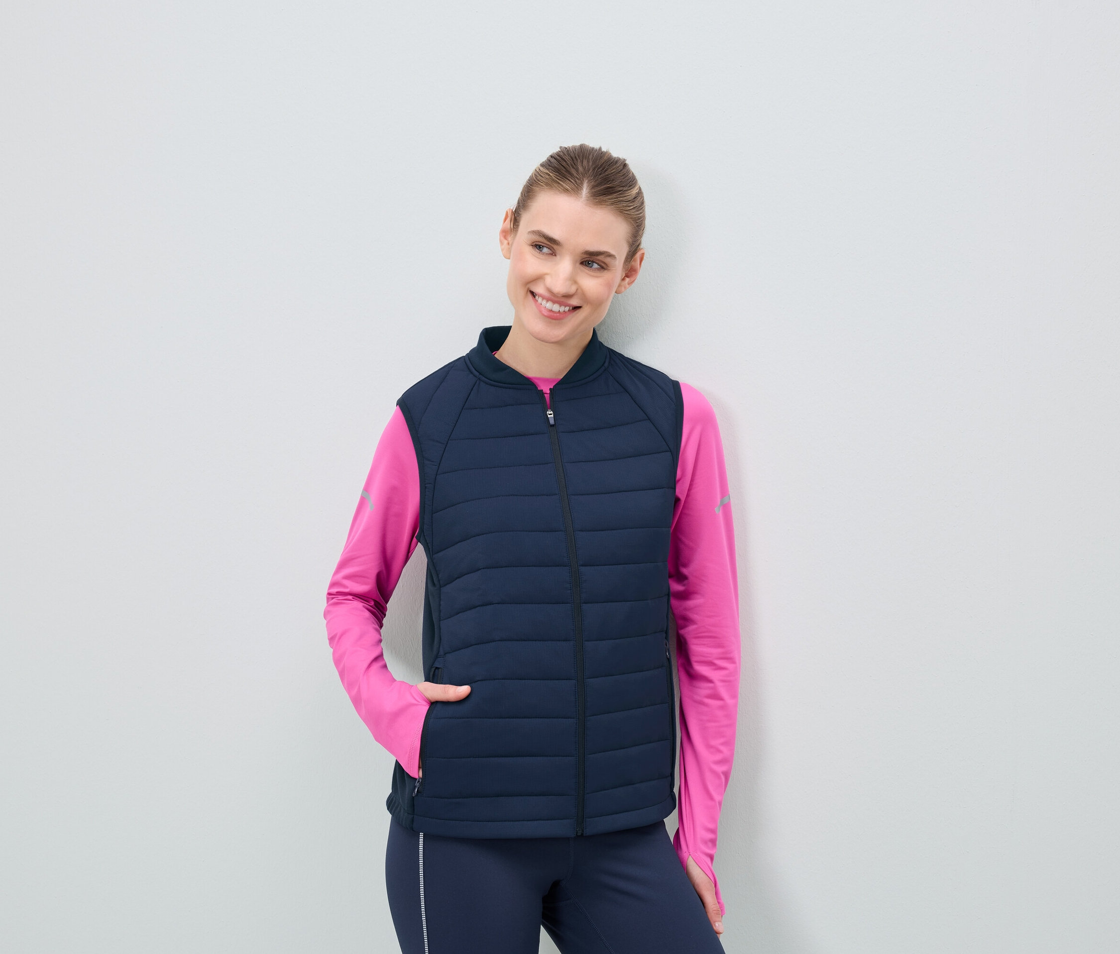 Kobieta w granatowej, pikowanej kamizelce i różowej bluzce z długim rękawem.
