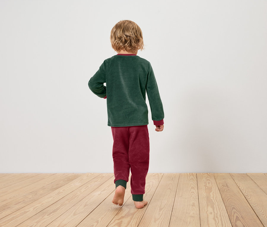 Chłopiec w zielonej piżamie i bordowych spodniach od piżamy idzie boso po drewnianej podłodze.