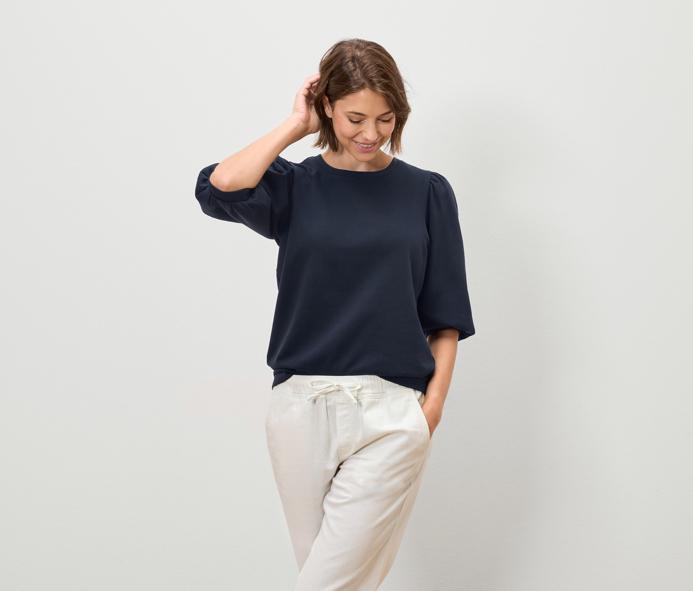 Kobieta pozuje w granatowej bluzce z krótkim rękawem i jasnych spodniach.