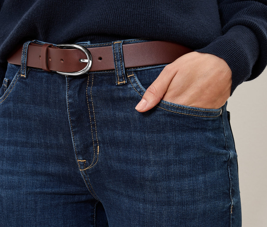 Zbliżenie na niebieskie dżinsy z koniakowym skórzanym paskiem.