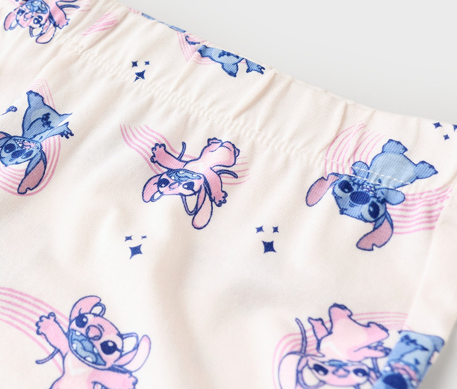 Zbliżenie na legginsy w beżowym kolorze z wzorem Stitch w kolorze niebieskim i różowym.